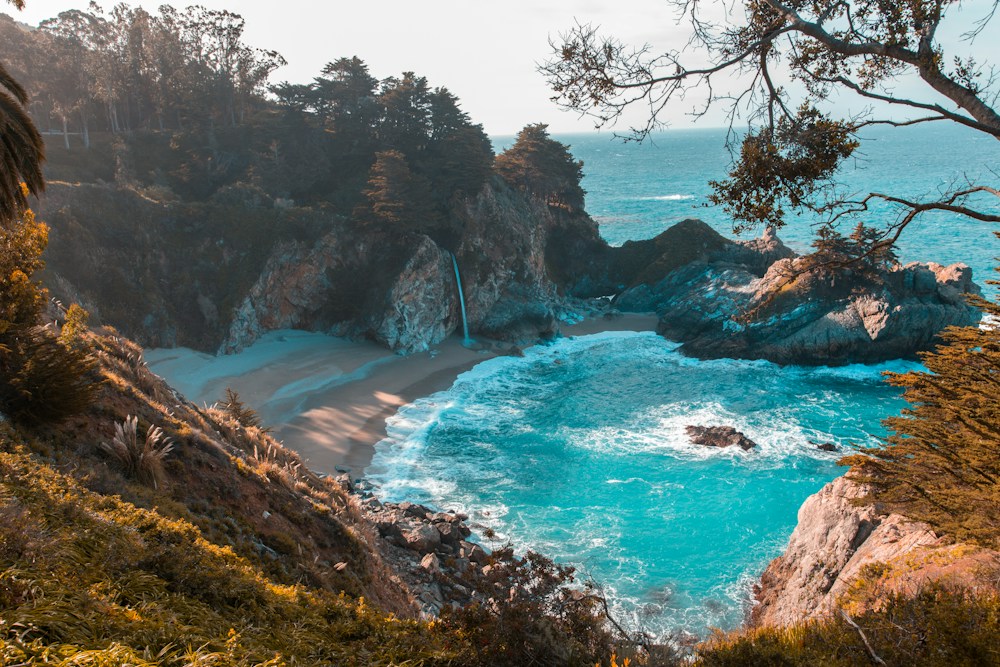 A secluded coastal cove surrounded by cliffs, trees, and blue water